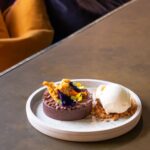 Decadent salted caramel chocolate tart topped with honeycomb shards, edible flowers, and served with vanilla ice cream on biscuit crumble — summer dessert at Racks Bar and Kitchen, Clifton, Bristol.
